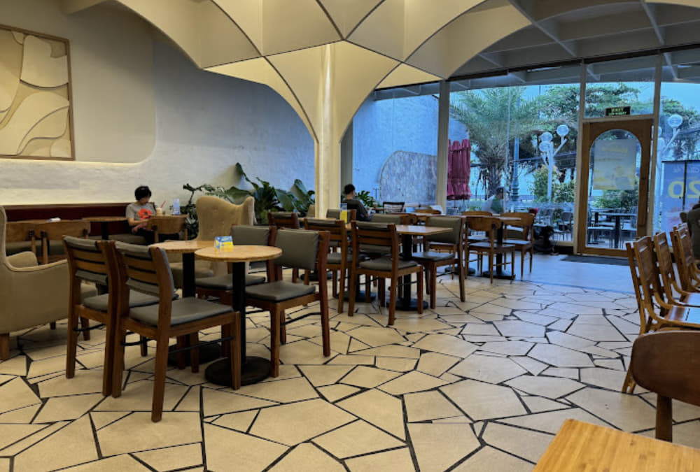 Khám Phá 12+ Quán Cafe Ngắm Hoàng Hôn Tuyệt Đẹp Tại Vũng Tàu 13 Quán cà phê với bàn ghế gỗ, ánh sáng tự nhiên từ cửa kính, có người ngồi thư giãn và làm việc.