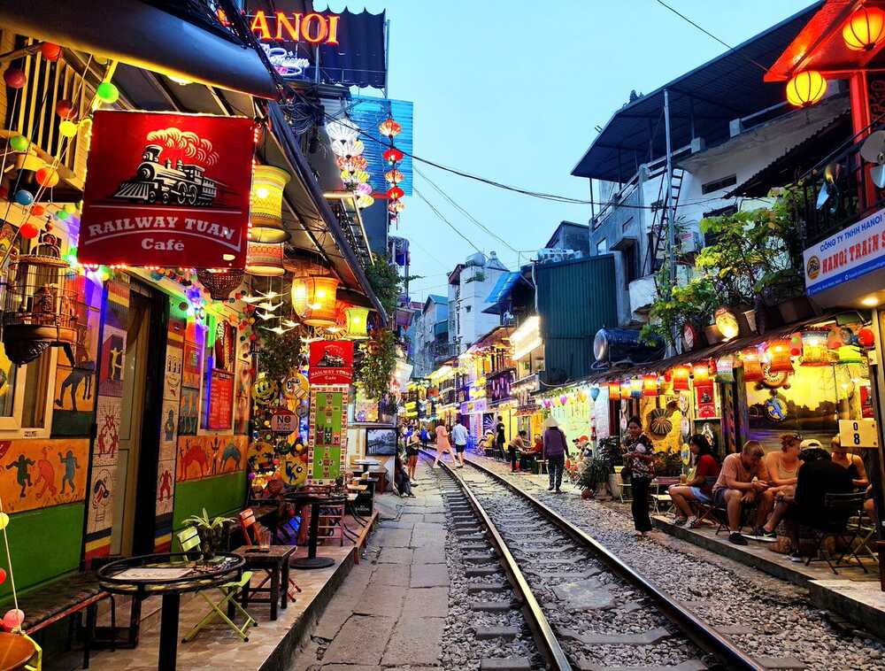 Khám Phá Phố Đường Tàu Phùng Hưng: Trải Nghiệm Cà Phê Độc Đáo Tại Hà Nội 5 Một con phố nhỏ với đường ray xe lửa, hai bên là quán cà phê và đèn lồng trang trí.