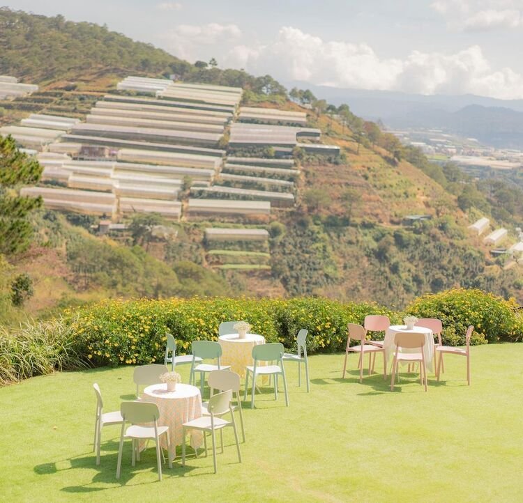 B&agrave;n ghế ngo&agrave;i trời tr&ecirc;n b&atilde;i cỏ xanh, nền l&agrave; nh&agrave; k&iacute;nh tr&ecirc;n đồi Đ&agrave; Lạt.