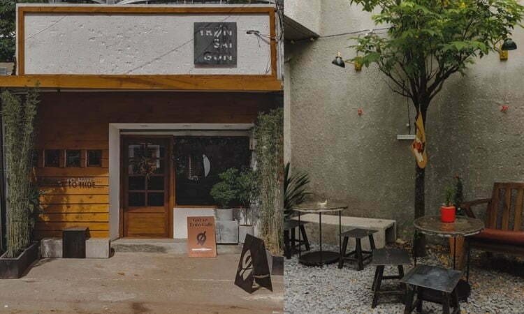 Mặt tiền qu&aacute;n c&agrave; ph&ecirc; với bảng hiệu tr&ecirc;n cao, b&ecirc;n ngo&agrave;i c&oacute; c&acirc;y v&agrave; b&agrave;n ghế ngồi ngo&agrave;i trời.