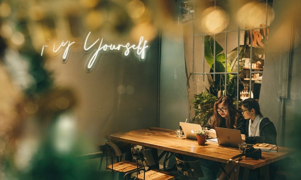 Khám Phá Top Quán Cafe Hấp Dẫn Trên Đường Nguyễn Chí Thanh - Điểm Đến Thú Vị 19 Hai người ngồi tại bàn gỗ trong quán cà phê, sử dụng máy tính xách tay, xung quanh là cây xanh và ánh đèn ấm áp.