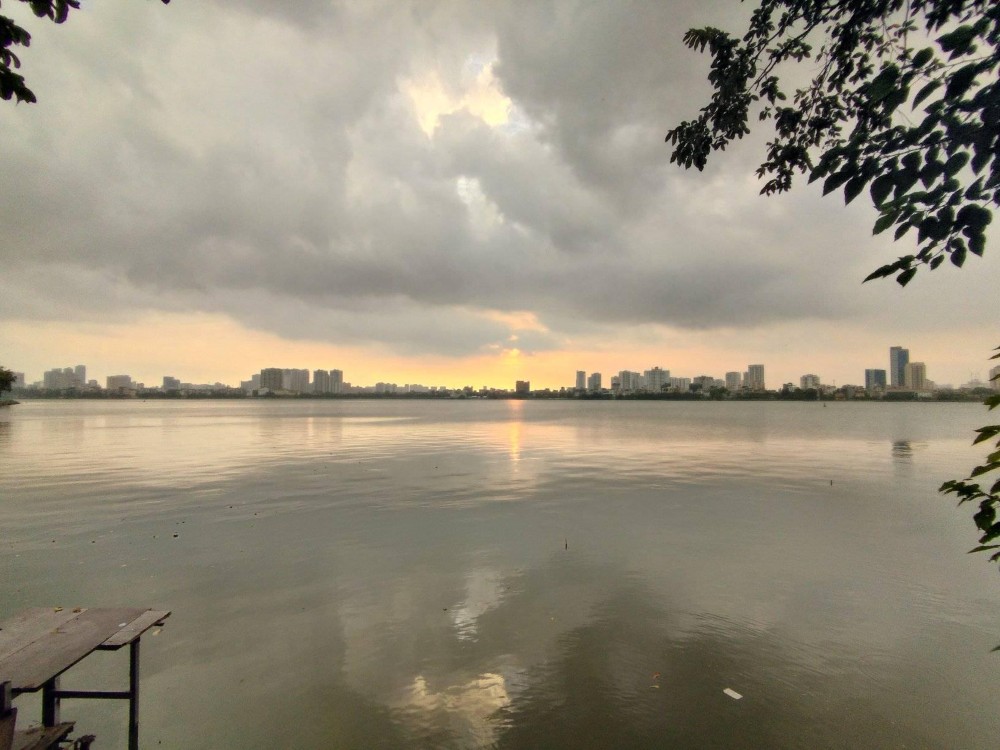 Khám Phá Top 10 Quán Cafe Hồ Tây View Đẹp Ngắm Hoàng Hôn Lãng Mạn 3 Hồ nước rộng lớn với bầu trời nhiều mây, có các tòa nhà cao tầng ở phía xa, khung cảnh hoàng hôn.