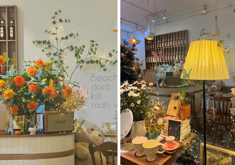 Quán cà phê ấm cúng với đèn vàng, hoa tươi sáng và sách bày trí tinh tế, tạo không gian thư giãn.