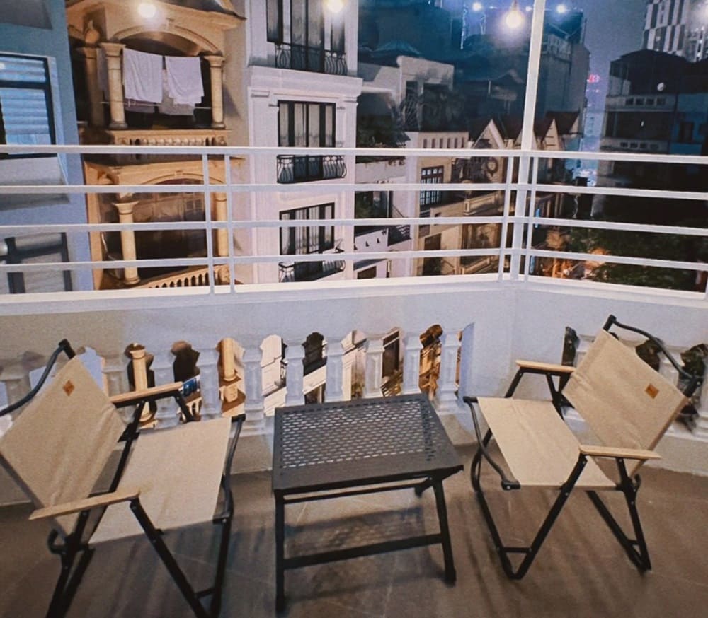 Top 9 Quán Cafe Phim Cầu Giấy Đáng Thử: Thưởng Thức Phim Hay, Cà Phê Ngon 13 Ban công với hai ghế và bàn nhỏ nhìn ra cảnh đêm thành phố với các tòa nhà sáng đèn.