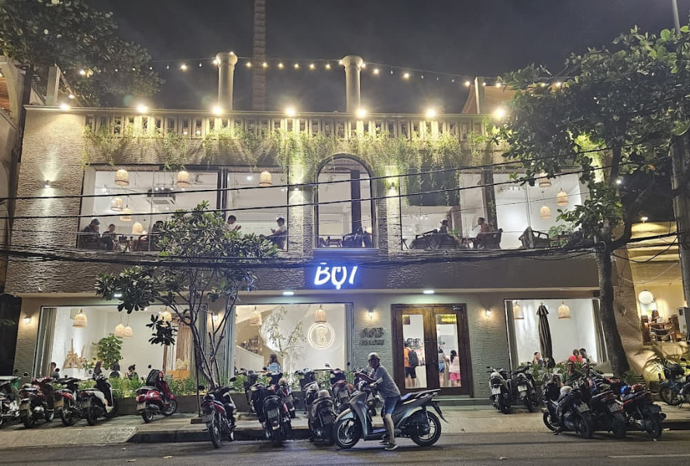 Khám Phá 12+ Quán Cafe Ngắm Hoàng Hôn Tuyệt Đẹp Tại Vũng Tàu 14 Quán cà phê hai tầng vào buổi tối với ánh đèn ấm áp, nhiều xe máy đậu phía trước.