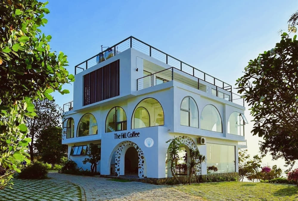 Khám Phá 12+ Quán Cafe Ngắm Hoàng Hôn Tuyệt Đẹp Tại Vũng Tàu 15 Quán cà phê hai tầng với thiết kế hiện đại, có nhiều cửa sổ lớn, được bao quanh bởi cây xanh.