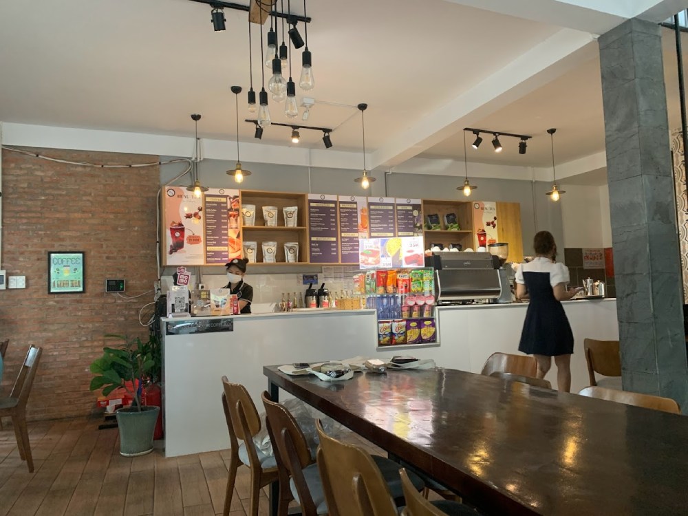 Khám Phá 8+ Quán Cafe Đêm Sài Gòn Đẹp Lung Linh Bạn Không Thể Bỏ Lỡ 9 Quán cà phê với quầy pha chế, thực đơn treo tường, bàn ghế gỗ, và hai người đang làm việc.