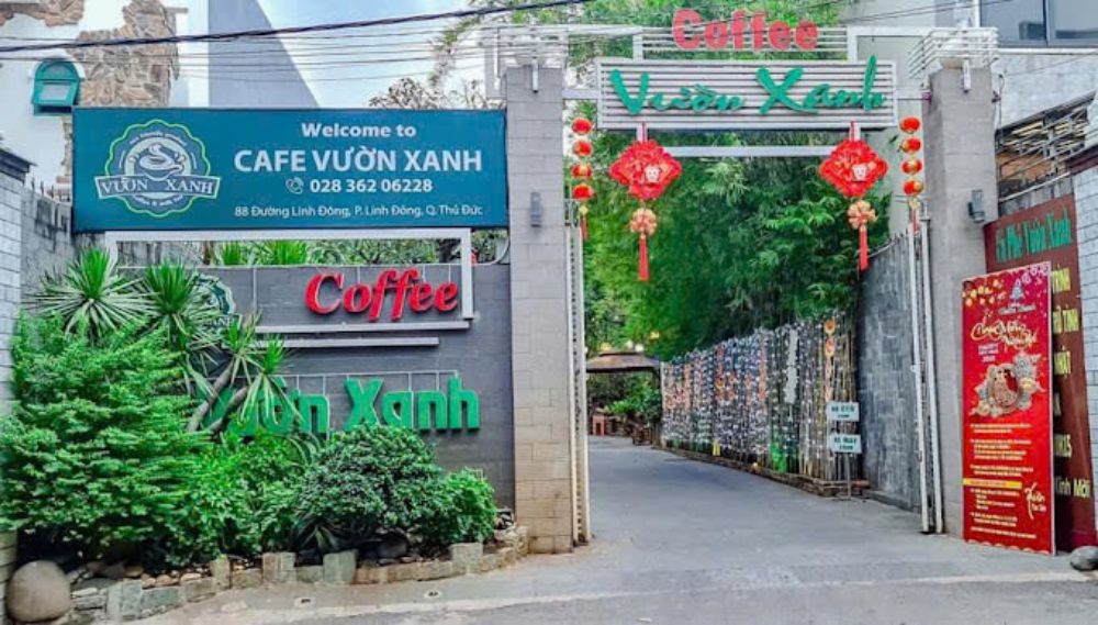 Khám Phá Top 10 Quán Cafe Sân Vườn Đẹp và Thư Giãn Tại Thủ Đức 12 Lối vào quán cà phê với biển hiệu và trang trí đèn lồng đỏ, cây xanh hai bên đường.