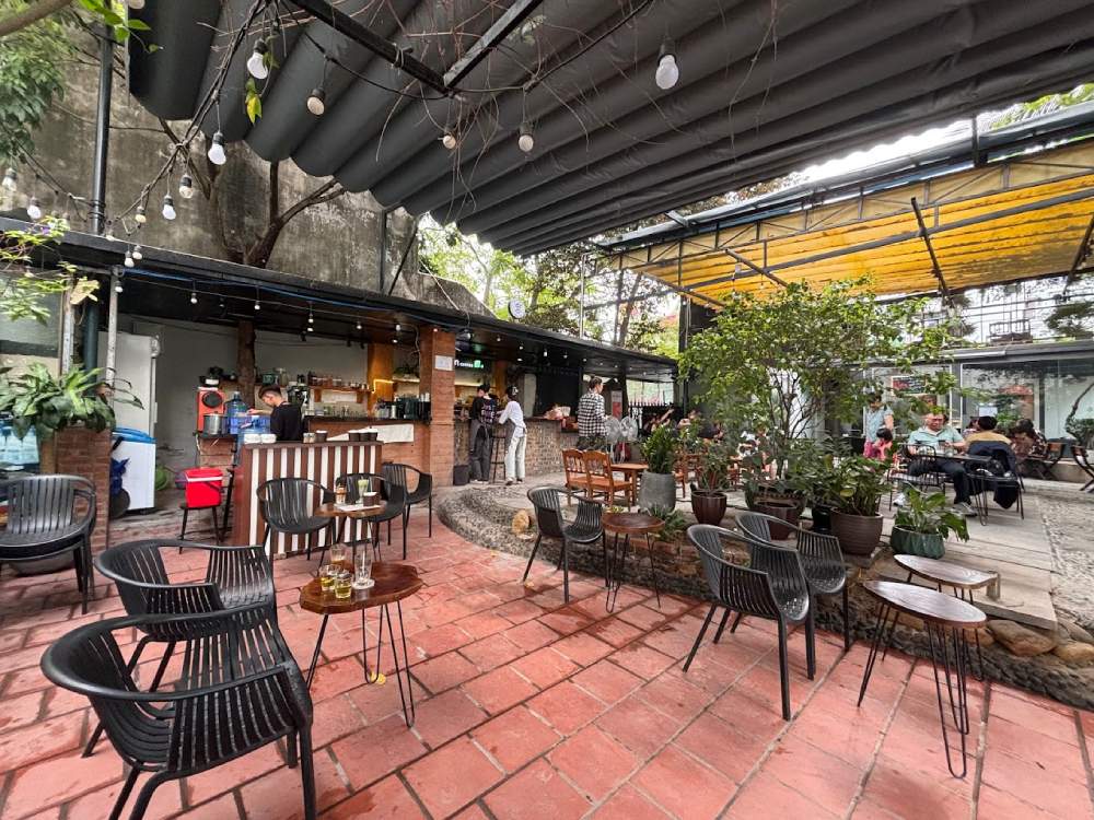 Khám Phá Garden Coffee Đội Cấn: Không Gian Yên Tĩnh Giữa Lòng Thủ Đô 4 Quán cà phê ngoài trời với bàn ghế, cây xanh và quầy pha chế. Khách hàng đang ngồi thưởng thức đồ uống.