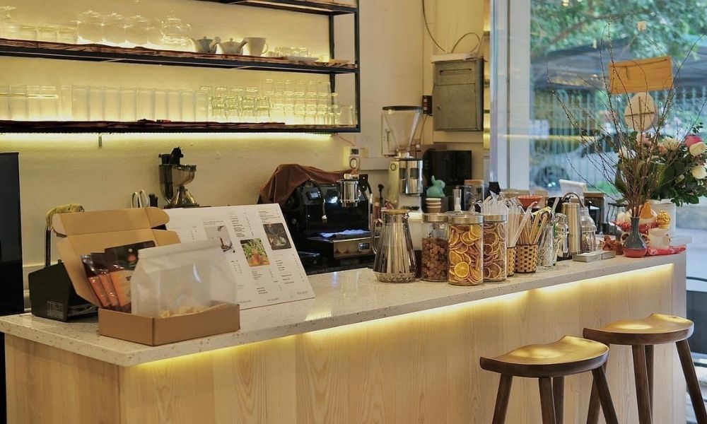 Khám Phá Top Quán Cafe Hấp Dẫn Trên Đường Nguyễn Chí Thanh - Điểm Đến Thú Vị 13 Quầy pha chế trong quán cà phê với máy pha cà phê, hũ đựng nguyên liệu và ghế ngồi.