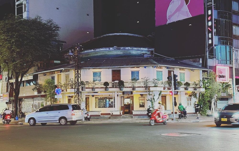 12 Quán Cafe Sài Gòn Xưa Hấp Dẫn Nhất định Phải Thử 9 Tòa nhà hai tầng ở góc phố, có cây xanh và xe cộ di chuyển vào buổi tối.