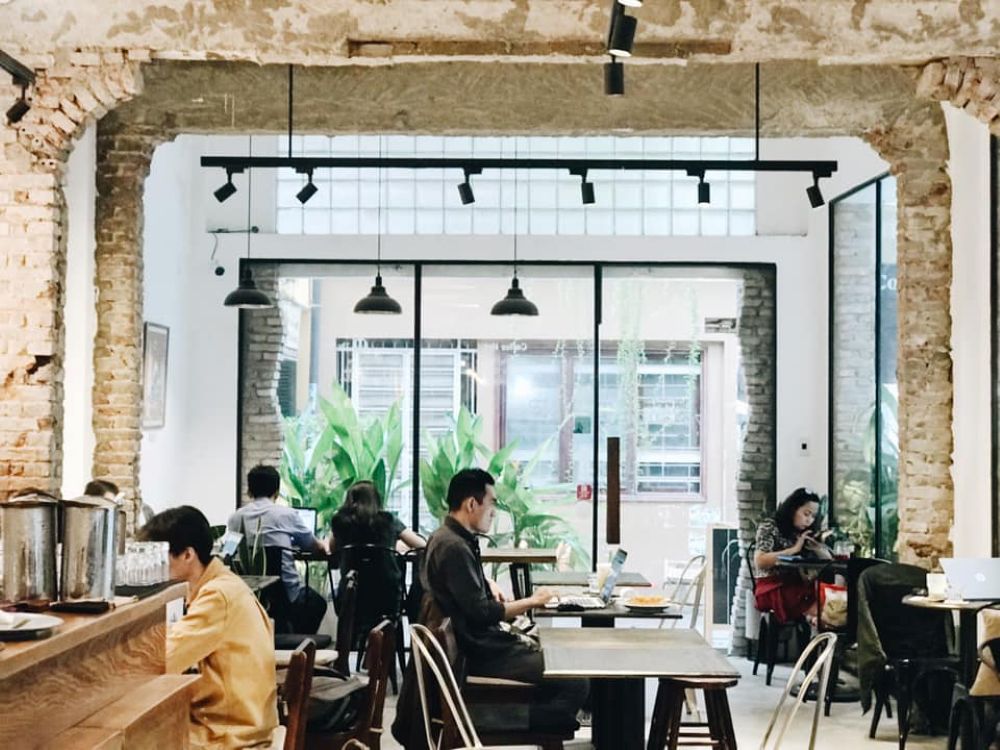 Khám Phá Top 10 Quán Cà Phê Yên Tĩnh Quận 3 Lý Tưởng Cho "Chạy Deadline" 27 Quán cà phê có không gian mở, tường gạch thô, nhiều người ngồi làm việc và trò chuyện.