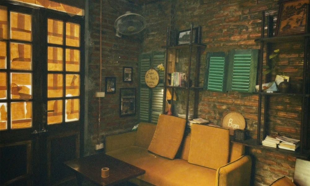 Khám Phá Top 6 Quán Cà Phê Trịnh Hấp Dẫn Tại Cầu Giấy 9 Phòng khách nhỏ có ghế sofa màu vàng, cửa kính, kệ sách và trang trí tường bằng gạch đỏ.