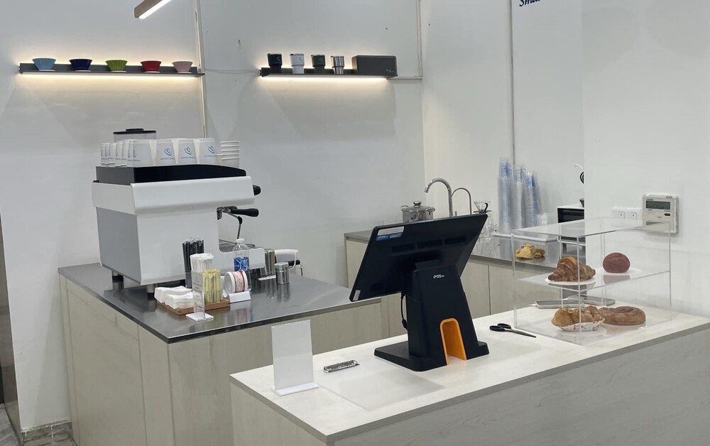 Quầy pha chế cà phê hiện đại với máy pha cà phê, bánh ngọt và quầy thanh toán.