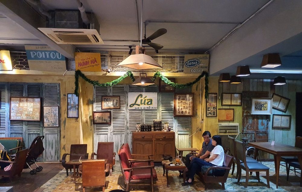 12 Quán Cafe Sài Gòn Xưa Hấp Dẫn Nhất định Phải Thử 7 Quán cà phê phong cách retro với nội thất gỗ và trang trí vintage, hai người ngồi trò chuyện trên ghế.