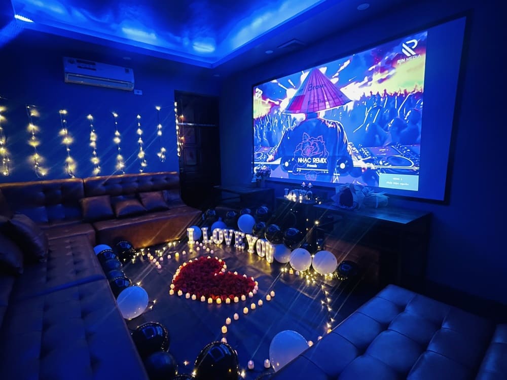 Top 9 Quán Cafe Phim Cầu Giấy Đáng Thử: Thưởng Thức Phim Hay, Cà Phê Ngon 8 Phòng karaoke trang trí ánh đèn xanh, nến và bóng bay, trên màn hình chiếu một DJ đang biểu diễn.