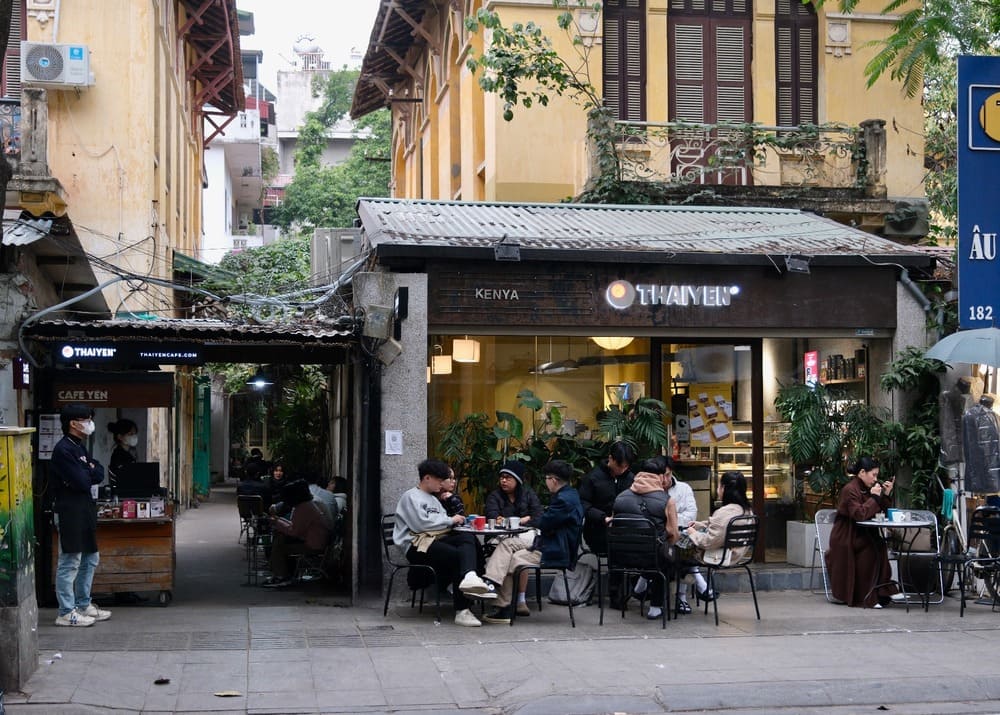 Quán cà phê ngoài trời ở Hà Nội, khách hàng ngồi uống cà phê, khung cảnh phố cổ với kiến trúc truyền thống.
