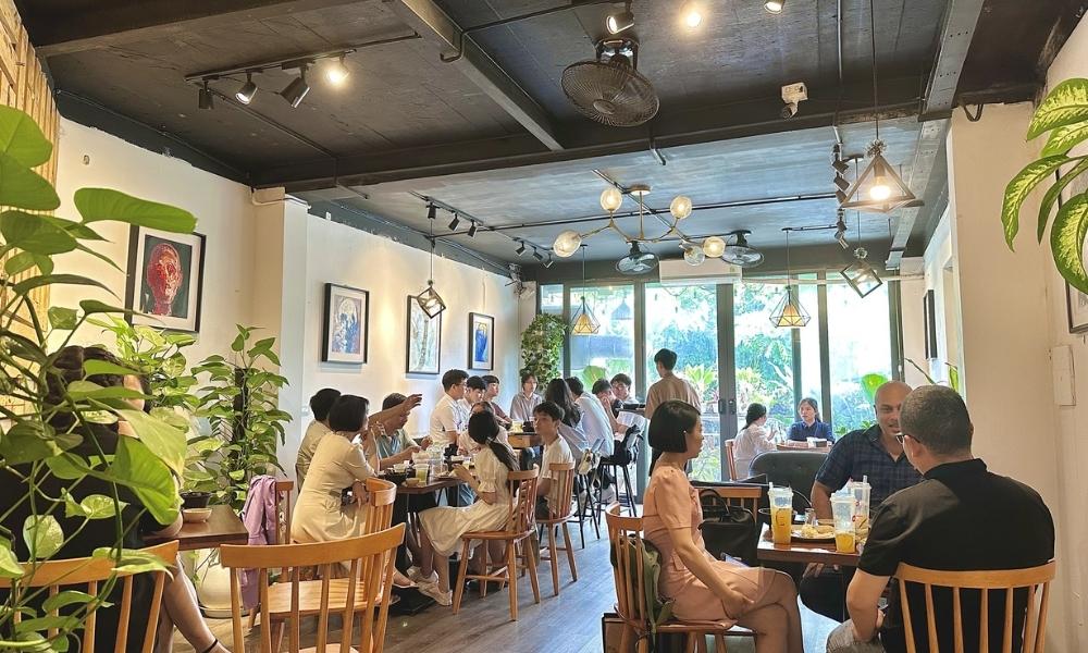 Khám Phá Top Quán Cafe Hấp Dẫn Trên Đường Nguyễn Chí Thanh - Điểm Đến Thú Vị 17 Quán cà phê với nhiều người đang trò chuyện, trang trí cây xanh và tranh treo tường, ánh sáng tự nhiên từ cửa sổ.