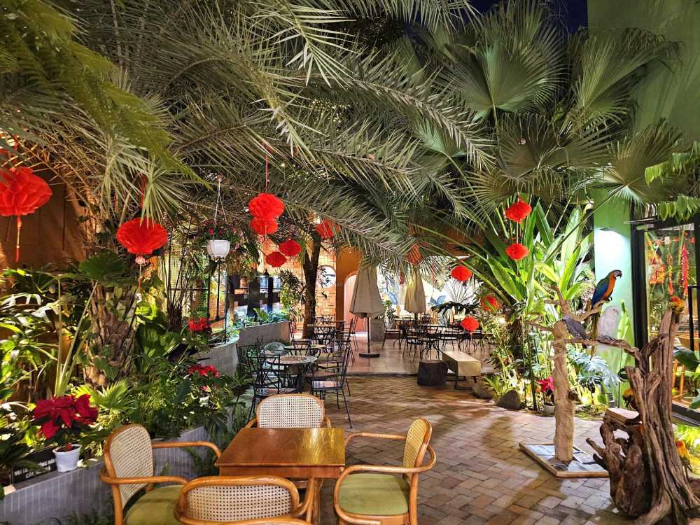Khám Phá 8 Quán Cafe Mèo TPHCM: Thiên Đường Cho Tín Đồ Yêu Mèo 6 Quán cà phê ngoài trời với cây cối xanh mát, đèn lồng đỏ trang trí và bàn ghế sắp xếp gọn gàng.