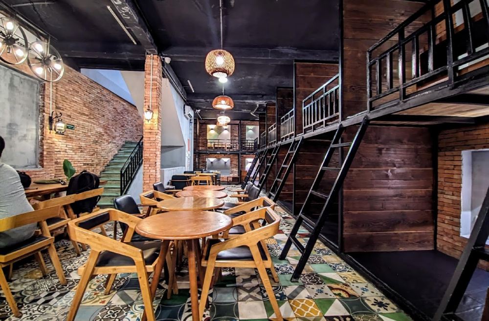 Khám Phá 8+ Quán Cafe Đêm Sài Gòn Đẹp Lung Linh Bạn Không Thể Bỏ Lỡ 15 Quán cà phê với bàn ghế gỗ, tường gạch đỏ và sàn hoa văn, có gác lửng và cầu thang.