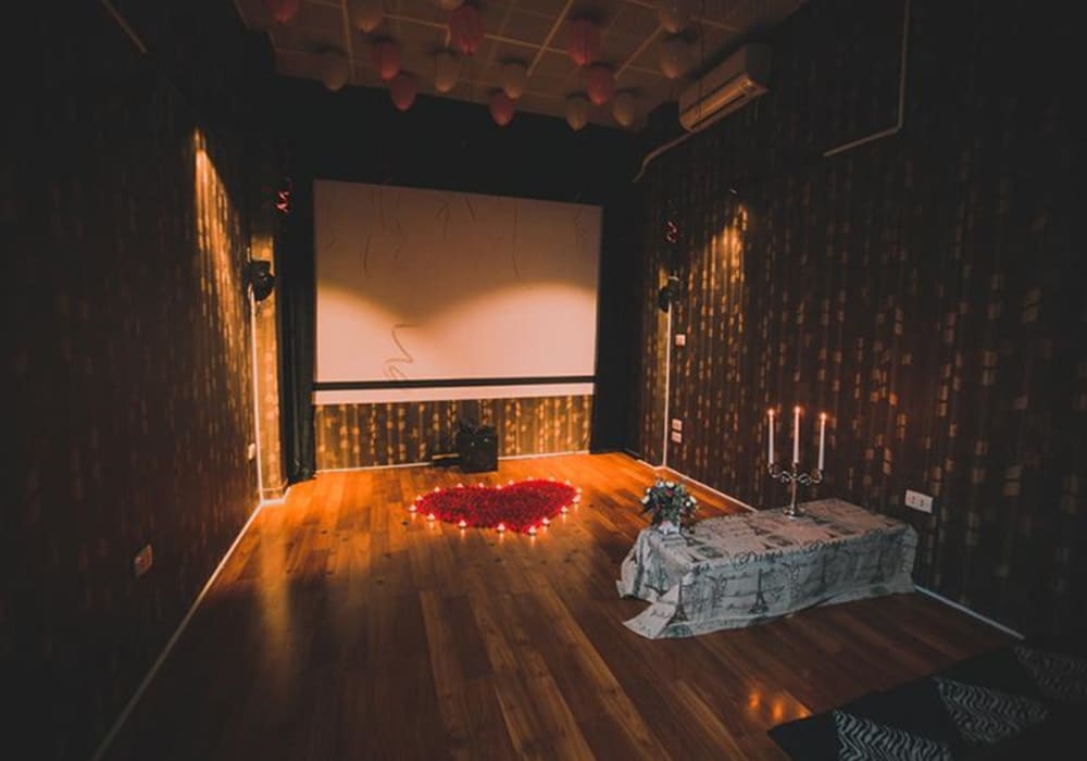 Top 9 Quán Cafe Phim Cầu Giấy Đáng Thử: Thưởng Thức Phim Hay, Cà Phê Ngon 21 Phòng trang trí với nến, hoa hồng thành hình trái tim, màn hình lớn trên tường, ánh sáng nhẹ nhàng.