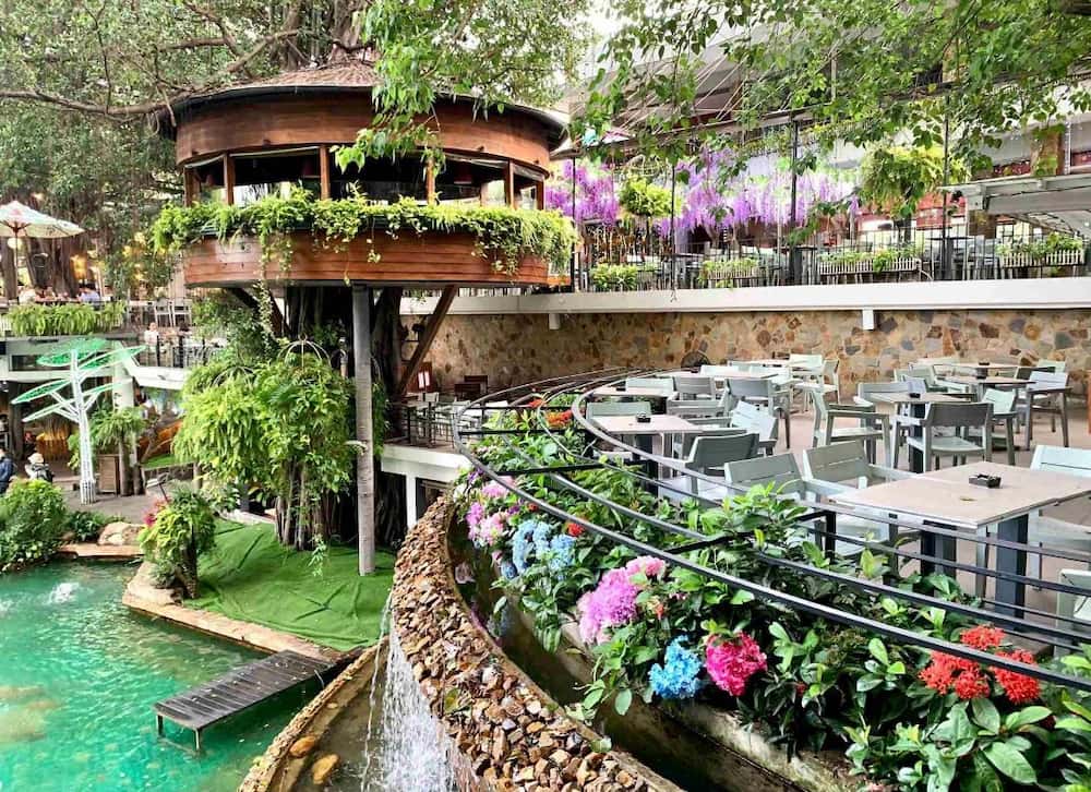 Khám Phá Du Miên Garden Cafe: Địa Điểm Độc Đáo Ngắm Sài Gòn Từ Trên Cao 5 Quán cà phê ngoài trời với nhà cây, bàn ghế, cây xanh và thác nước nhỏ, tạo không gian xanh mát.
