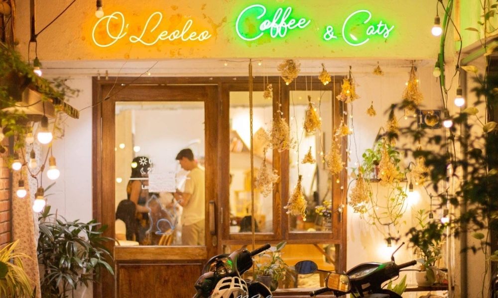 Khám Phá Top Quán Cafe Hấp Dẫn Trên Đường Nguyễn Chí Thanh - Điểm Đến Thú Vị 7 Mặt tiền quán cà phê với bảng hiệu đèn neon và trang trí cây xanh, bên trong có khách ngồi.