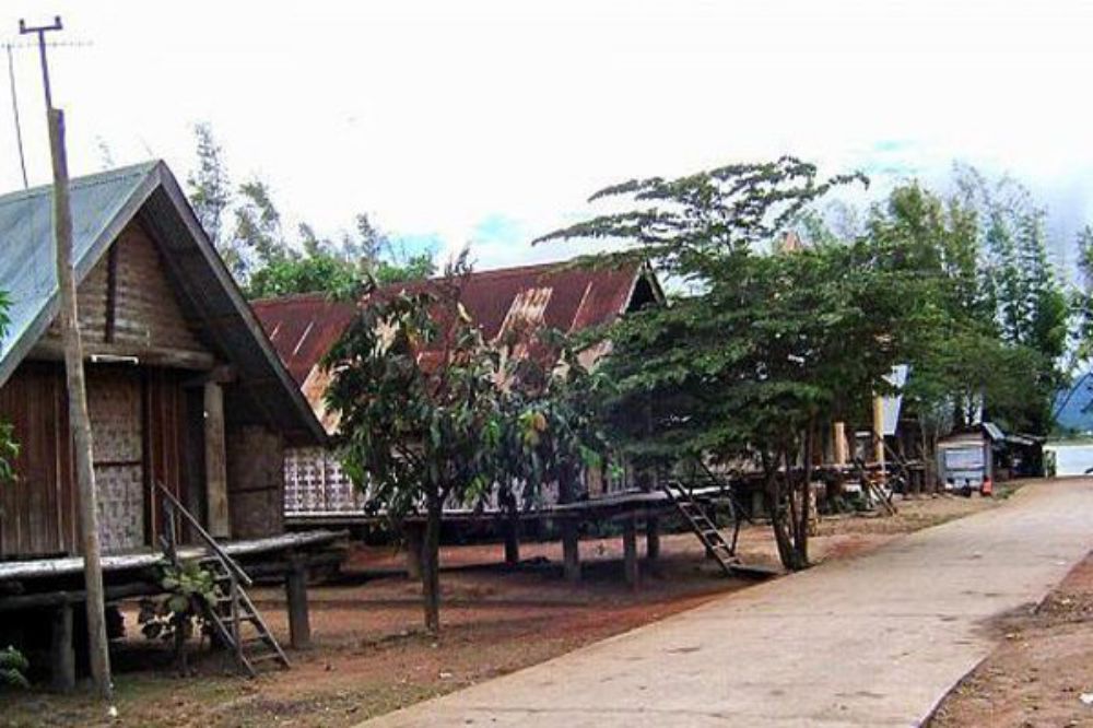 Những ngôi nhà sàn bằng gỗ nằm dọc con đường nhỏ, xung quanh có cây cối xanh tươi.