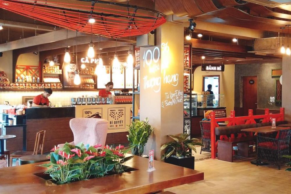 Khám Phá 10+ Quán Cafe Đẹp Nhất Long Biên: Thỏa Sức “Sống Ảo”, Thưởng Thức Đồ Uống Ngon 3 Quán cà phê với nội thất ấm cúng, có quầy pha chế, bàn ghế, cây trang trí và ánh sáng đèn vàng dịu nhẹ.