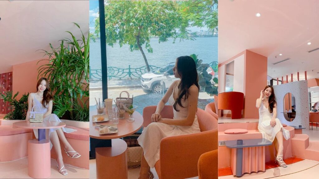 Khám Phá Top 10 Quán Cafe Hồ Tây View Đẹp Ngắm Hoàng Hôn Lãng Mạn 13 Người phụ nữ ngồi trong quán cà phê với nội thất màu hồng, bên cửa sổ nhìn ra ngoài có cây và xe hơi.
