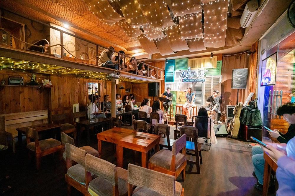 12 Quán Cafe Sài Gòn Xưa Hấp Dẫn Nhất định Phải Thử 16 Một quán cà phê với sân khấu nhạc sống, nhiều người ngồi nghe nhạc, trang trí ánh sáng ấm áp, nội thất gỗ.