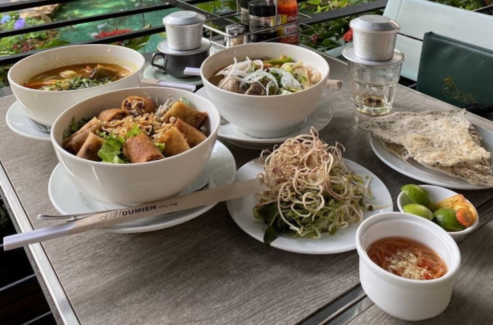 Khám Phá Du Miên Garden Cafe: Địa Điểm Độc Đáo Ngắm Sài Gòn Từ Trên Cao 8 Bàn ăn với các món Việt Nam như phở, bún chả giò, bánh đa, rau sống và ly cà phê phin.