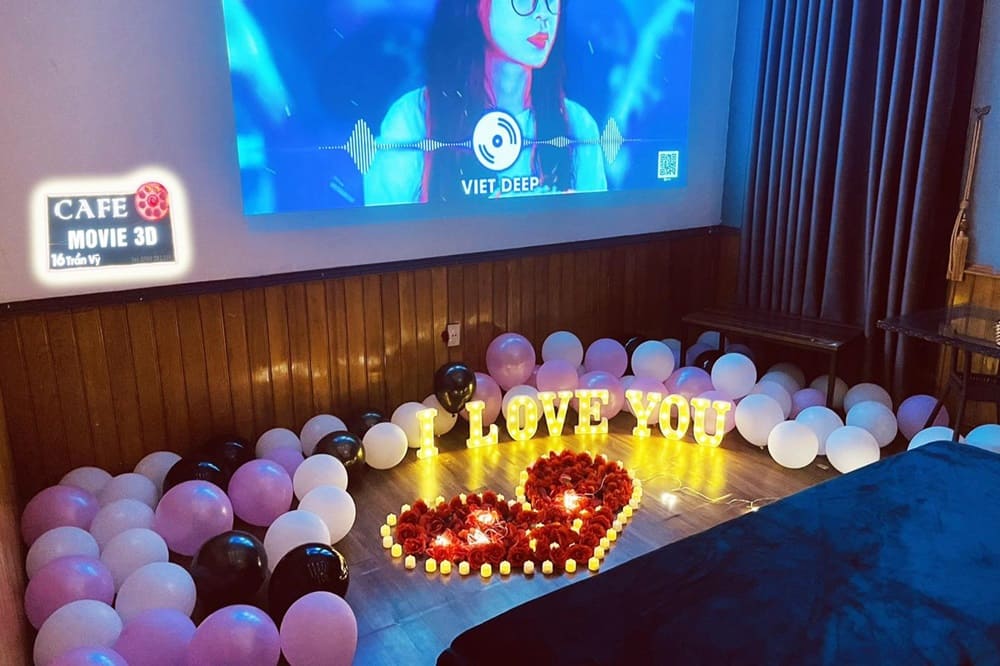 Top 9 Quán Cafe Phim Cầu Giấy Đáng Thử: Thưởng Thức Phim Hay, Cà Phê Ngon 3 Phòng chiếu phim trang trí bóng bay và đèn chữ "I LOVE YOU", với màn hình hiển thị hình ảnh ca sĩ.