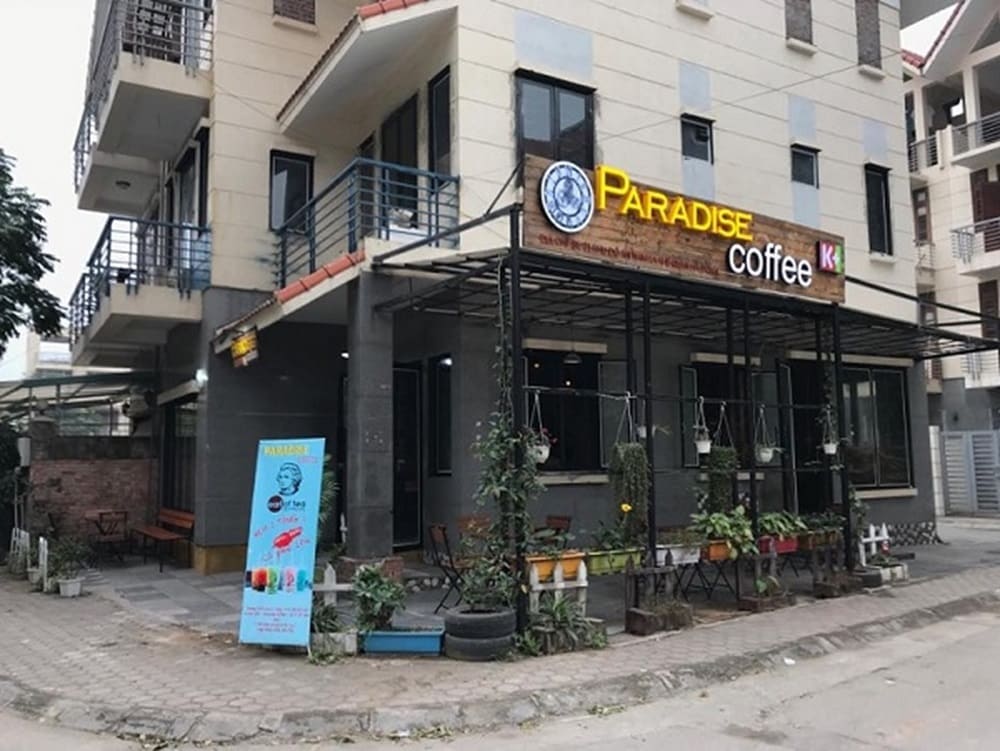 Top 9 Quán Cafe Phim Cầu Giấy Đáng Thử: Thưởng Thức Phim Hay, Cà Phê Ngon 17 Quán cà phê góc phố với biển hiệu "Paradise Coffee" và cây xanh trang trí phía trước.