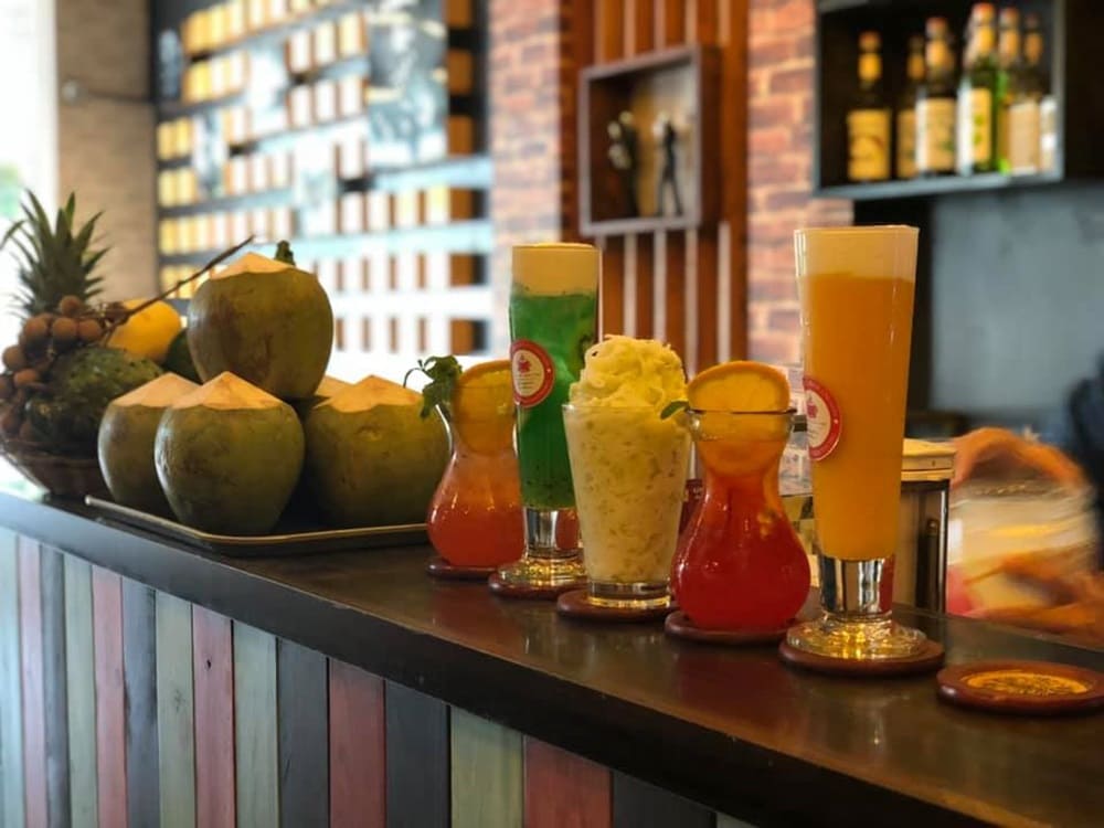 Top 9 Quán Cafe Phim Cầu Giấy Đáng Thử: Thưởng Thức Phim Hay, Cà Phê Ngon 5 Các loại đồ uống và trái dừa được bày trên quầy bar với phông nền là kệ gỗ và chai lọ.