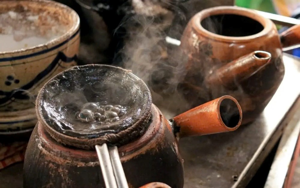 Khám Phá Top 6+ Quán Cà Phê Vỉa Hè Sài Gòn Được Giới Trẻ Yêu Thích 4 Ấm đất đang sôi trên bếp, hơi nước bốc lên, bên cạnh là một chiếc bát sứ và một ấm đất khác.