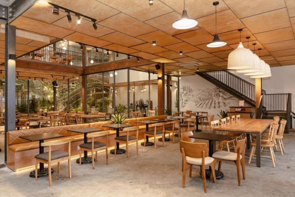Khám Phá 10+ Quán Cafe Đẹp Nhất Long Biên: Thỏa Sức “Sống Ảo”, Thưởng Thức Đồ Uống Ngon 6 Quán cà phê hiện đại với bàn ghế gỗ, đèn treo trang trí và cầu thang dẫn lên tầng trên.