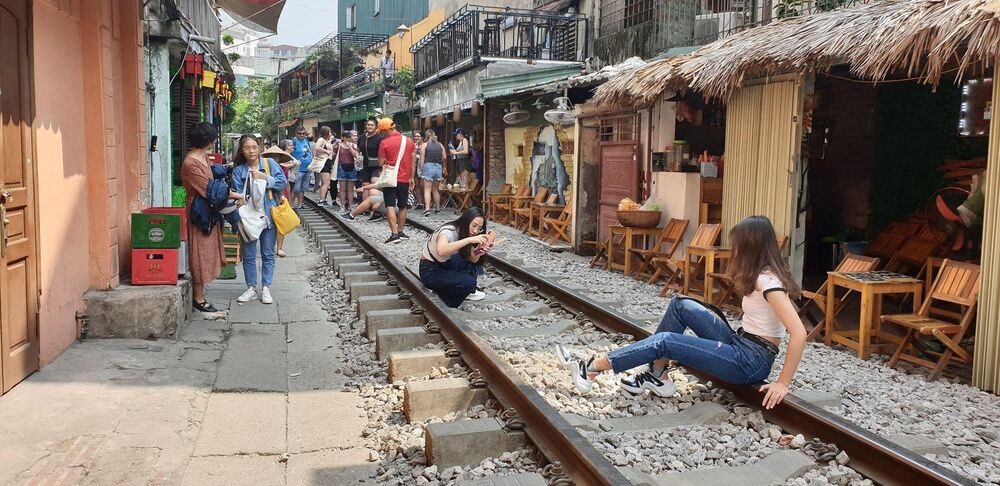 Khám Phá Phố Đường Tàu Phùng Hưng: Trải Nghiệm Cà Phê Độc Đáo Tại Hà Nội 7 Du khách chụp ảnh và tham quan bên cạnh đường ray tại một khu phố với quán cà phê và hàng quán.