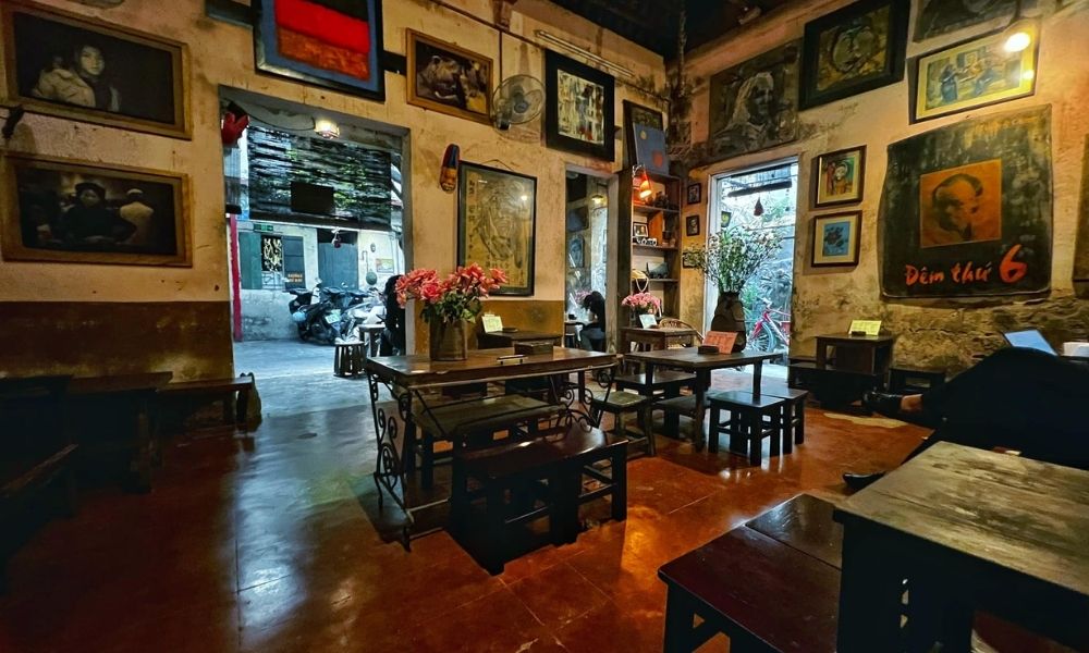 Khám Phá Top 6 Quán Cà Phê Trịnh Hấp Dẫn Tại Cầu Giấy 5 Quán cà phê với nội thất cổ điển, nhiều tranh treo tường và bàn ghế gỗ, lối ra dẫn đến khu vực ngoài trời.