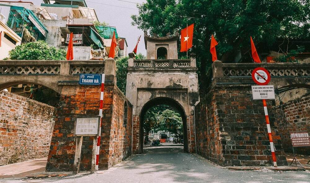 Khám Phá Phố Đường Tàu Phùng Hưng: Trải Nghiệm Cà Phê Độc Đáo Tại Hà Nội 9 Cổng đá cổ với cờ đỏ treo trên, bên cạnh có biển báo giao thông và biển tên đường Thanh Hà.