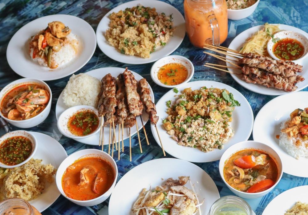 B&agrave;n ăn với nhiều m&oacute;n ăn đa dạng như cơm, thịt xi&ecirc;n, s&uacute;p v&agrave; c&aacute;c loại nước sốt, b&agrave;y tr&iacute; tr&ecirc;n nền xanh.