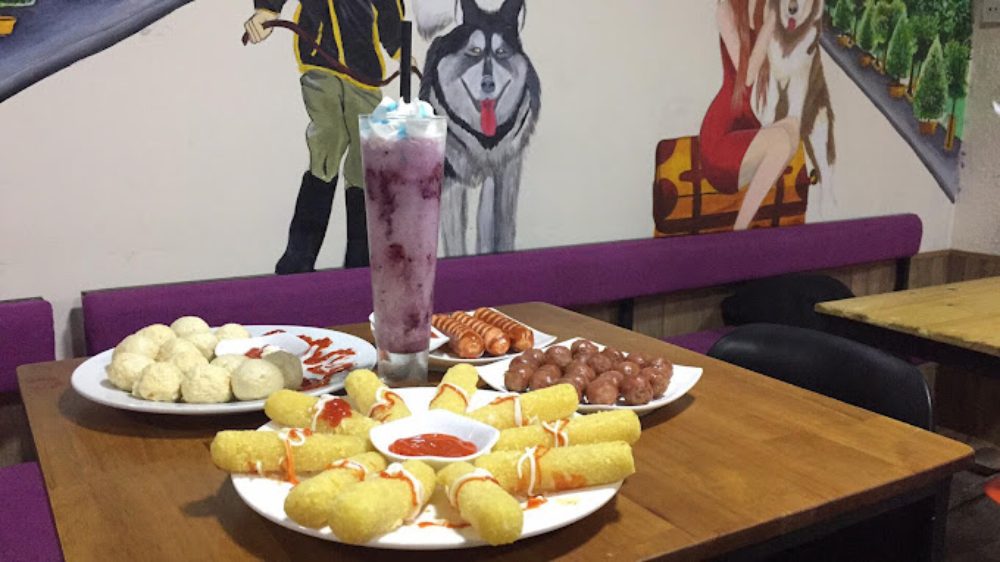 Khám Phá 8 Quán Cafe Mèo TPHCM: Thiên Đường Cho Tín Đồ Yêu Mèo 12 Bàn ăn với nhiều món ăn nhẹ và đồ uống, phía sau là bức tường có tranh vẽ trang trí.