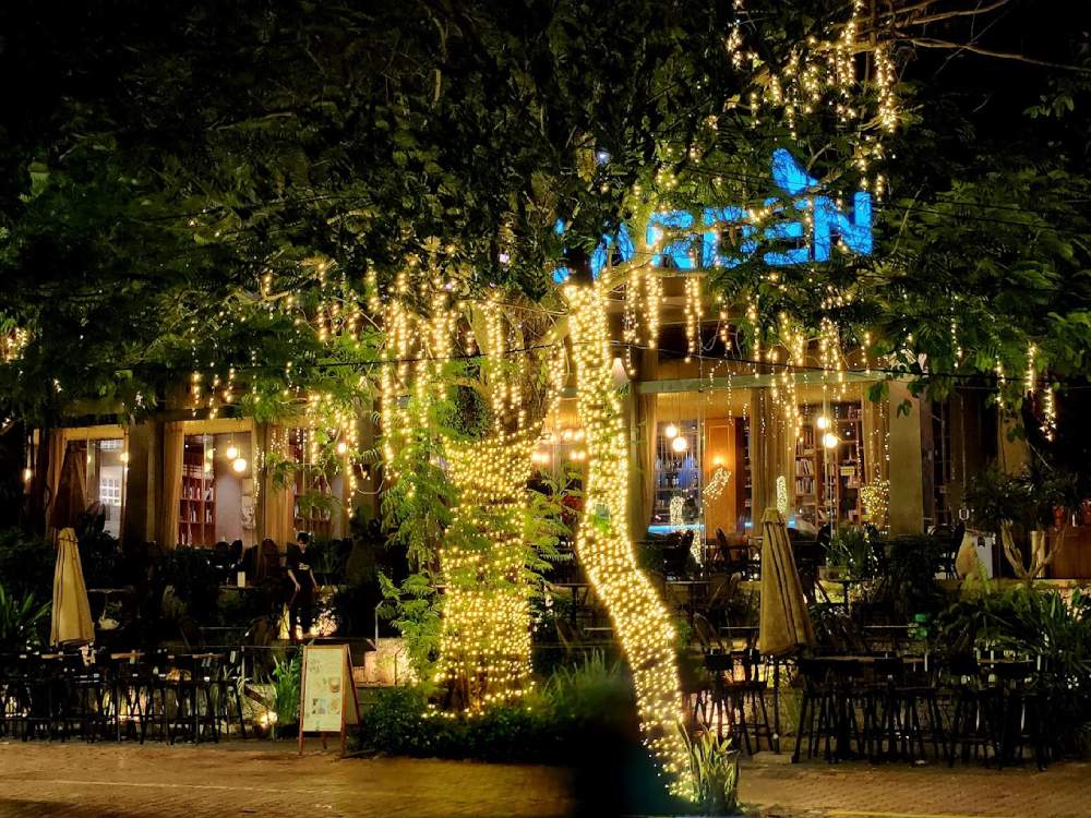 Top 11+ Quán Cafe Đẹp Tại Đà Nẵng Không Thể Bỏ Qua Năm 2025 12 Quán cà phê ngoài trời buổi tối, cây cối trang trí đèn lấp lánh, không gian ấm cúng và thư thái.