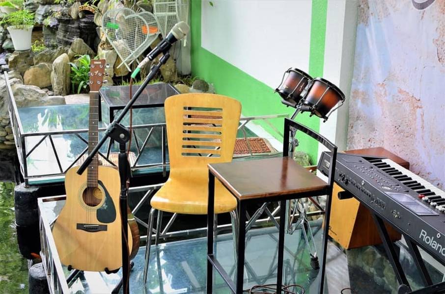 S&acirc;n khấu ngo&agrave;i trời với đ&agrave;n guitar, micro, trống v&agrave; đ&agrave;n ph&iacute;m điện tử, ph&iacute;a sau l&agrave; bức tường xanh v&agrave; c&acirc;y cối.