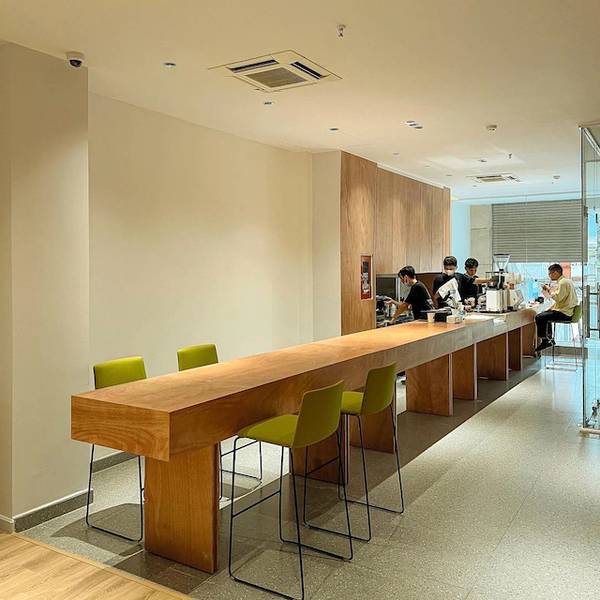 Qu&aacute;n c&agrave; ph&ecirc; hiện đại với quầy gỗ d&agrave;i v&agrave; kh&aacute;ch h&agrave;ng đang thưởng thức đồ uống.