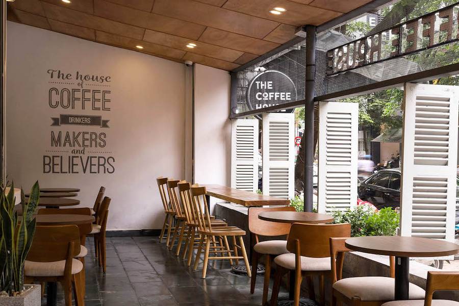 Qu&aacute;n c&agrave; ph&ecirc; ấm c&uacute;ng với b&agrave;n ghế gỗ v&agrave; c&acirc;y xanh, cửa sổ mở ra đường phố nhộn nhịp.