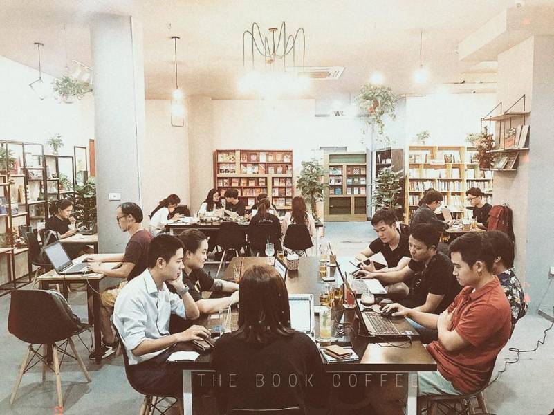 cafe-sach-ha-noi-11-1024x767-1 Quán cà phê với nhiều người ngồi làm việc trên laptop, xung quanh có kệ sách và cây cảnh trang trí.