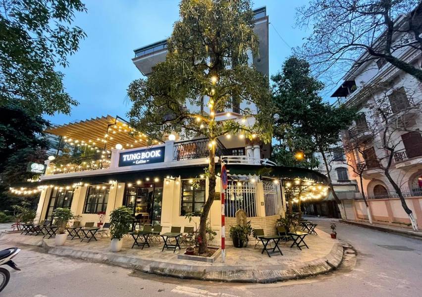 cafe-sach-ha-noi-18-1024x721-1 Quán cà phê với ánh đèn trang trí, bàn ghế ngoài trời, nằm ở góc phố, cây xanh xung quanh.