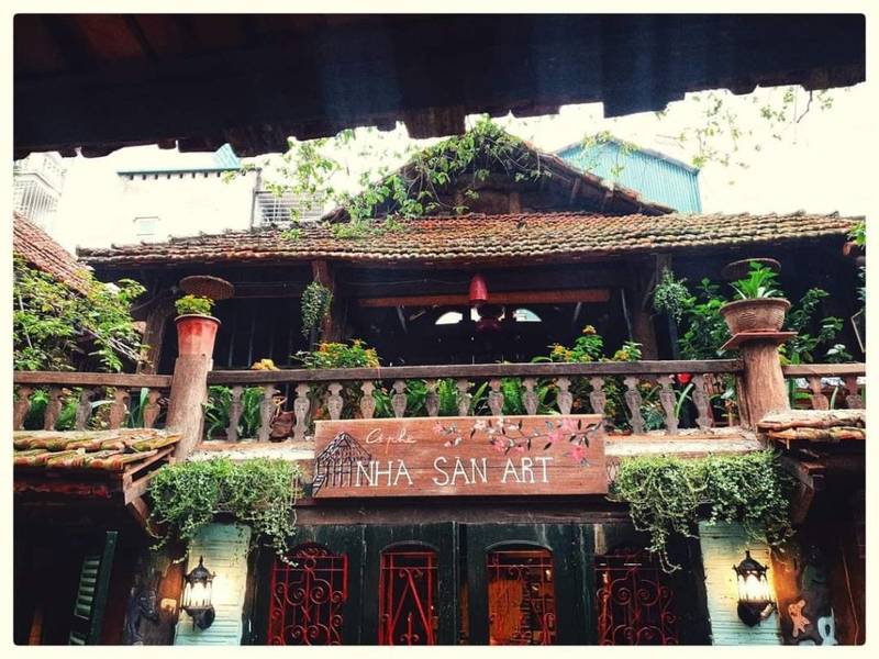 cafe-sach-ha-noi-18-1024x768-1 Ngôi nhà hai tầng bằng gỗ, trang trí cây xanh, biển hiệu ghi "Nhà Sàn Art", phong cách truyền thống.