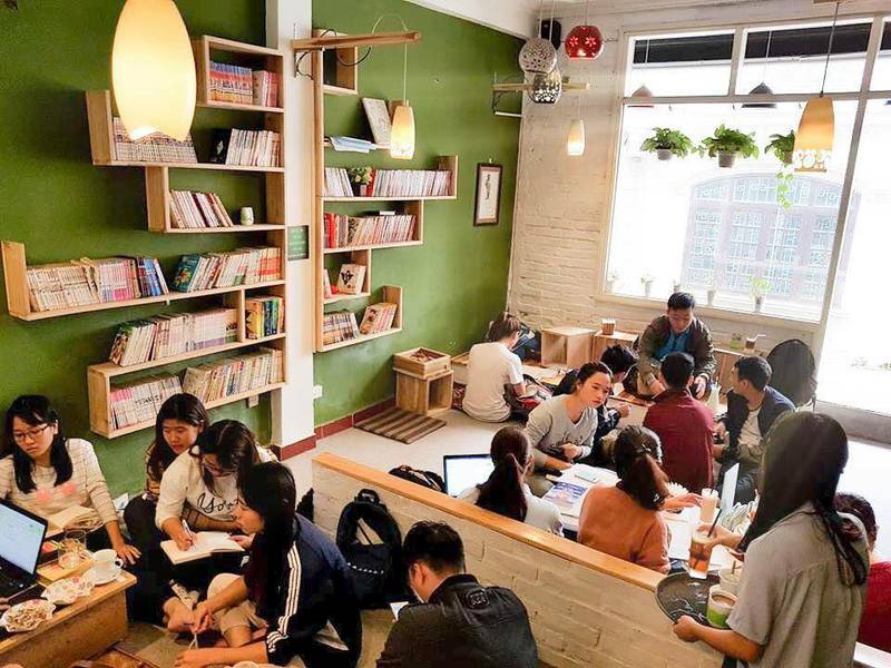 cafe-sach-ha-noi-20 Một nhóm người đang ngồi trong quán cà phê, trò chuyện và làm việc cùng nhau trên máy tính xách tay và sổ tay.